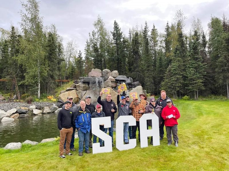 A reunion group gathered behind SCA letters in front of the waterfall
