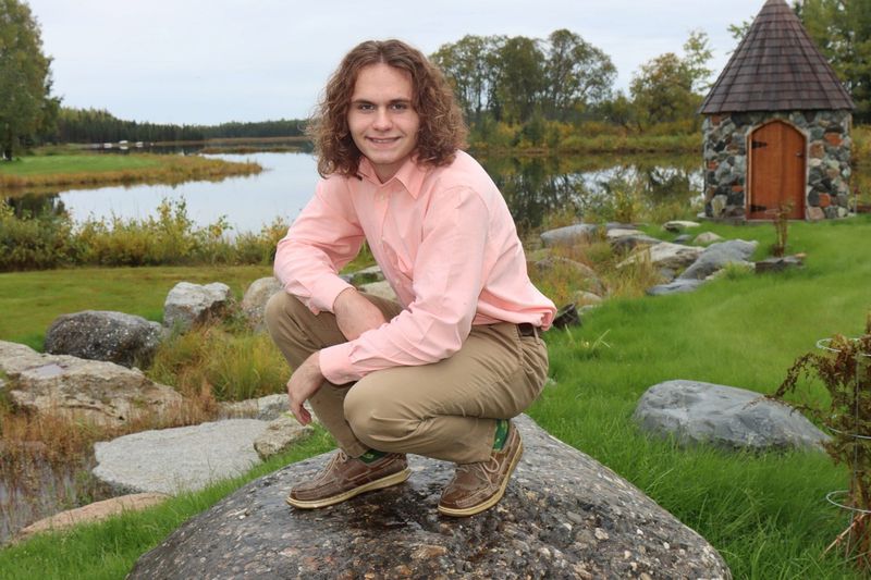 A young man crouching on a boulder by the lake