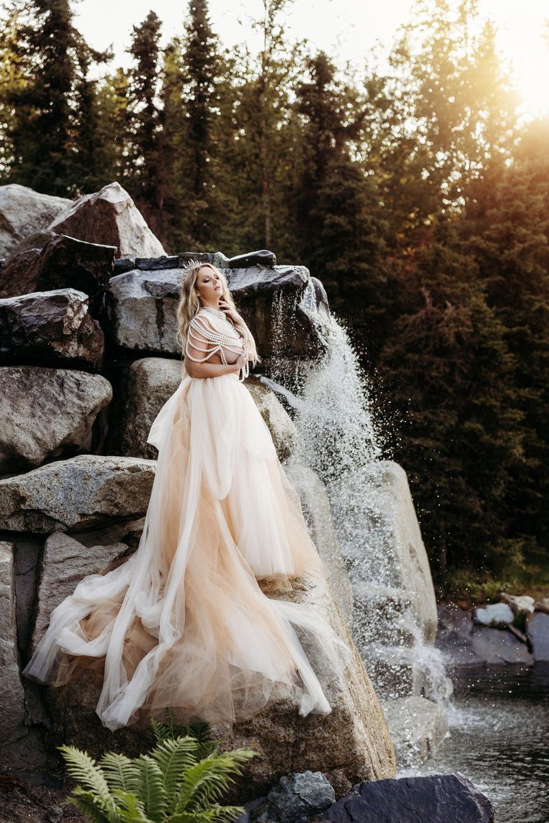 A bride in a flowing gown beside the waterfall at golden hour