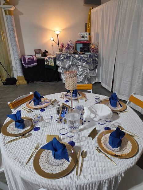 An indoor dinner table set with blue napkins and gold chargers